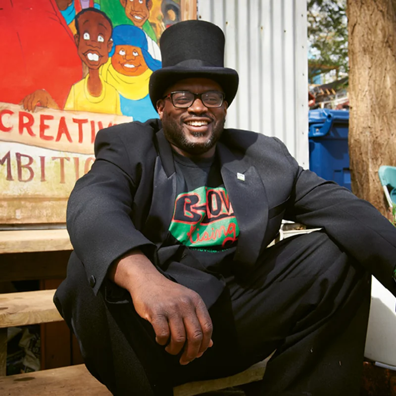 Dwayne Barton sits wearing a black suit and hat